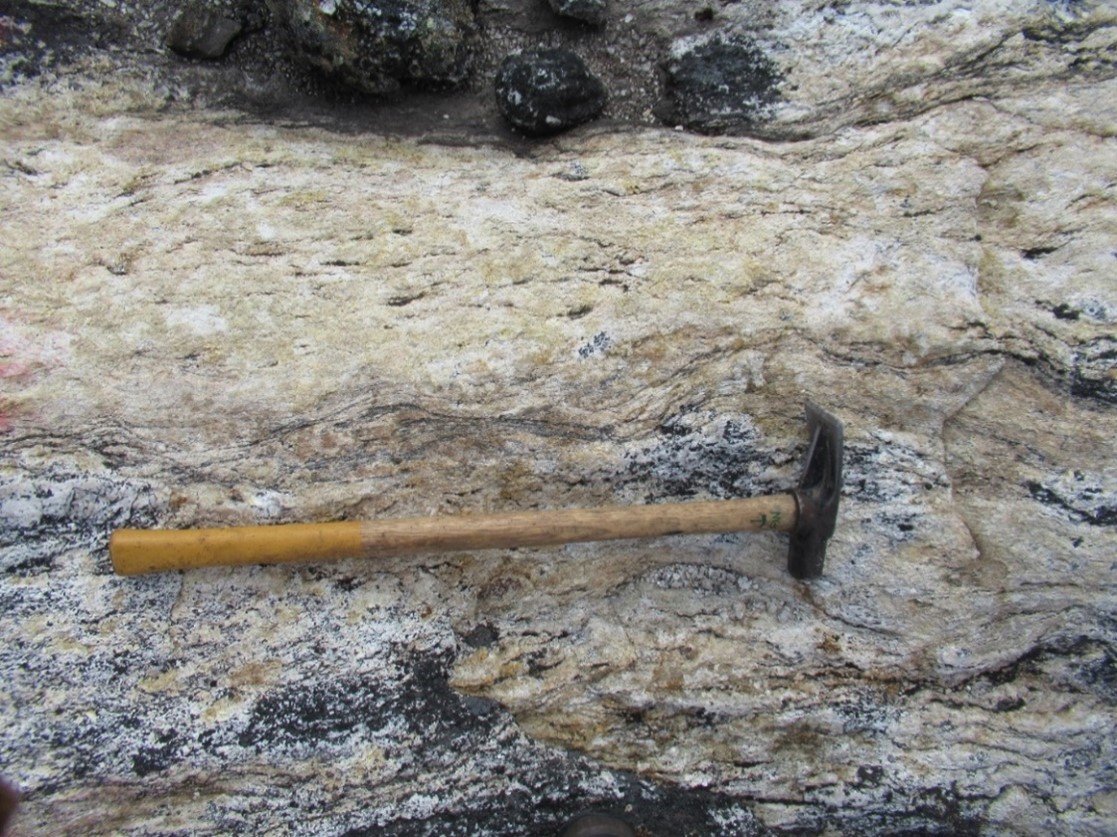 Highly strained granitic pegmatite showing an East-West foliation and significant uranophane mineralization located in the Katjuk (Arrow) Zone. Photo showing biotite fabric in the pegmatite with localised stringers of garnet beads.